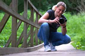 Fotografin Lisa Welling, junge Frau, hockt mit einer Kamera auf einer Holzbrücke.